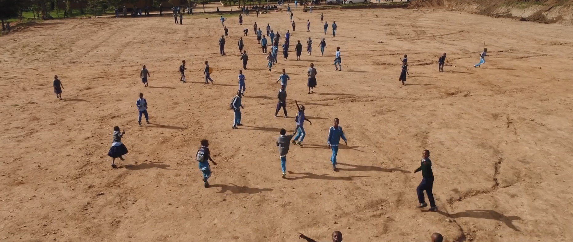 Aerial view of uniformed students running across a dirt school field in Africa