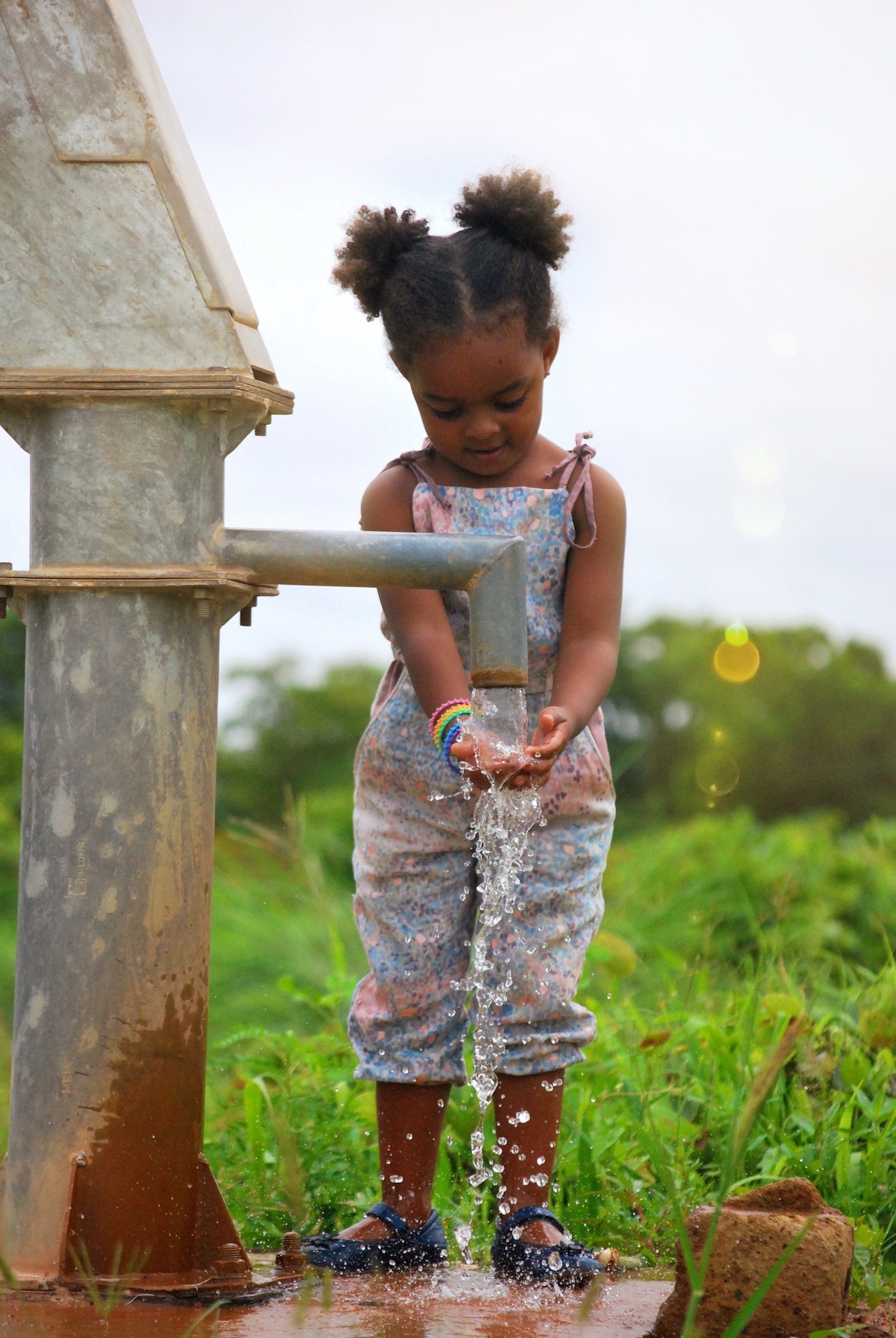 A young girl washing her hands at a water pump